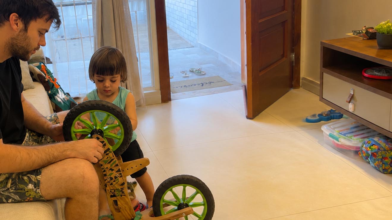 Pai e filha montando a bicicleta de madeira em casa