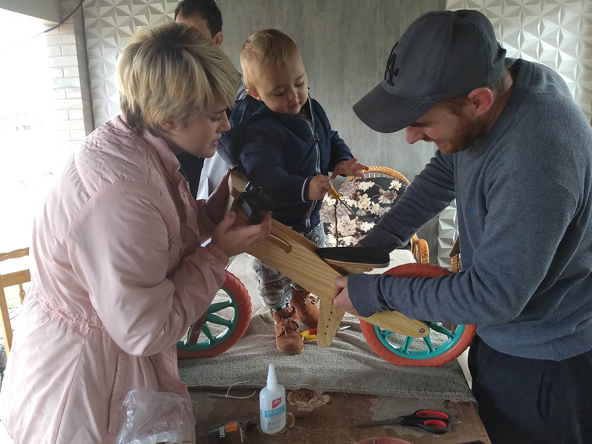 Depoimento da Pâmela: a mãe, o pai, o dindo e a criança montando juntos a Biciquetinha de rodas verdes