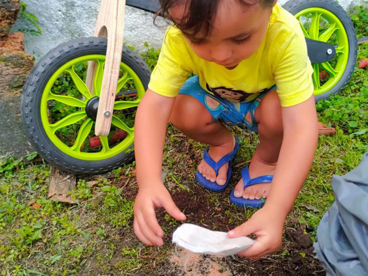 Criança plantando a semente de pitanga no jardim ao lado da Biciquetinha